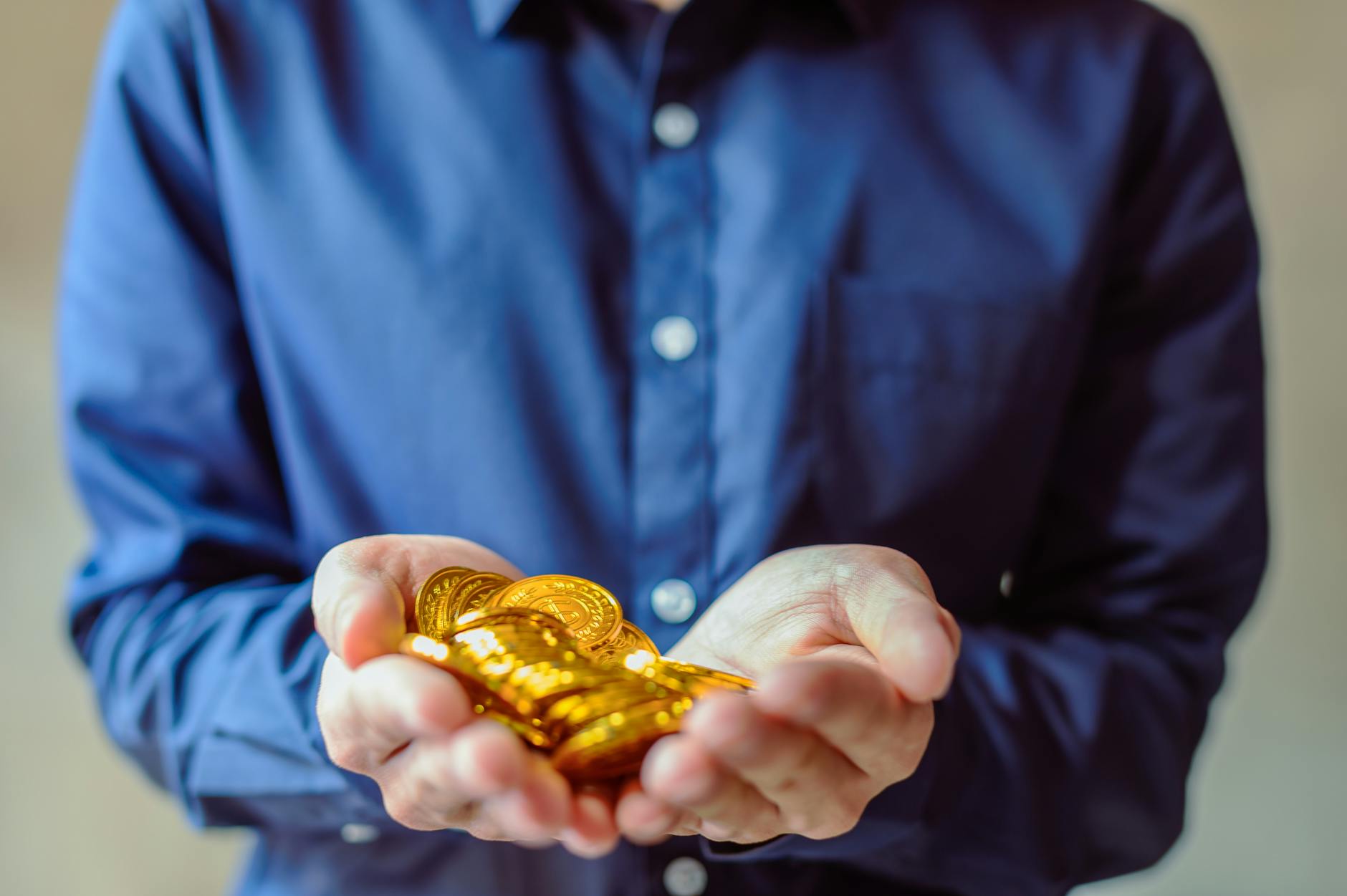 A person in a blue shirt holds a handful of shiny golden coins, symbolizing wealth and cryptocurrency.