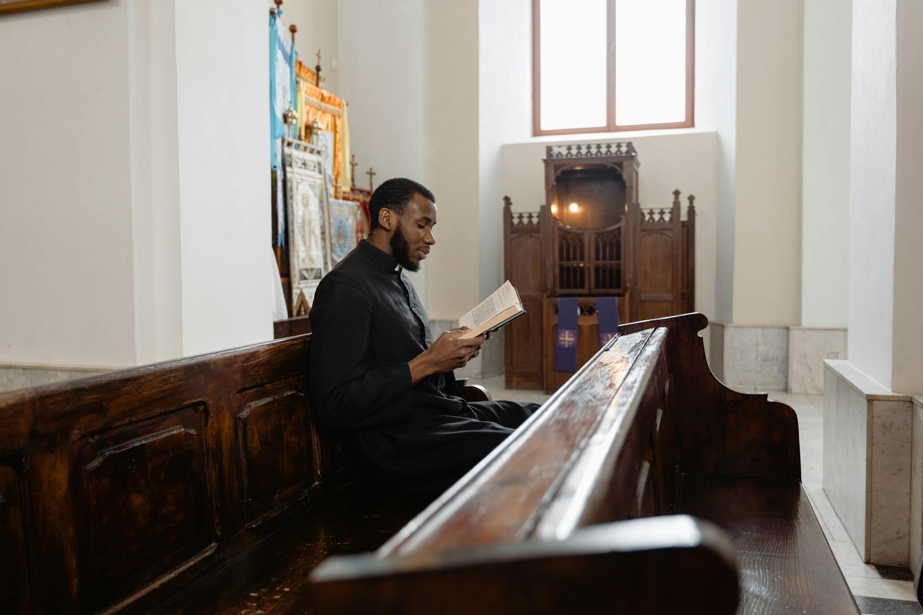 A priest in a vestment reading a Bible inside a peaceful church setting.